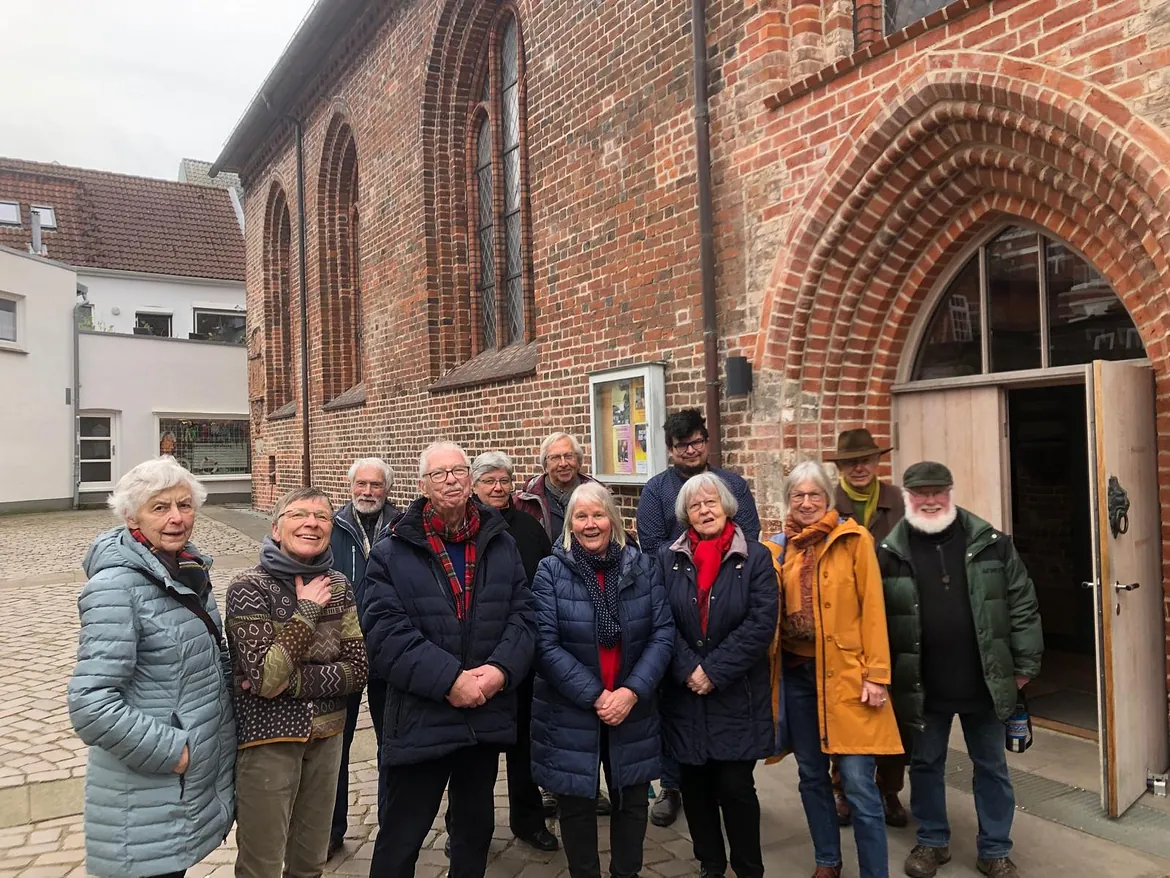 Seniorengruppe versammelt sich draußen vor einem roten Backsteinkirchengebäude.